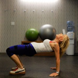 Woman doing a reverse plank exercise in a gym setting.