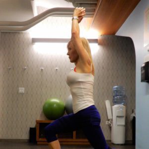 Woman in athletic wear stretches indoors with arms raised.
