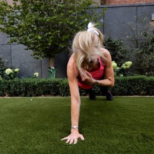 Woman exercising outdoors on green grass, performing a plank with arm extension.