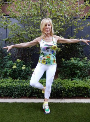 Woman practicing yoga balance pose outdoors in a garden.