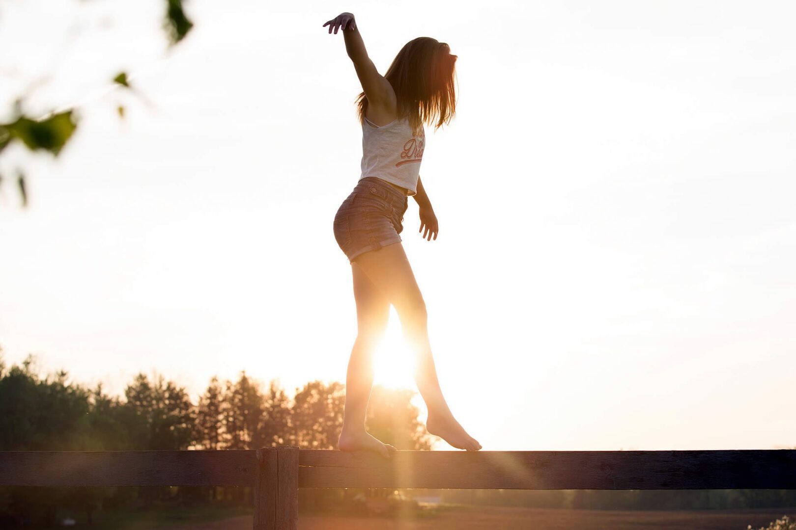 Woman balancing on a rail during sunset with sunlight glowing behind.