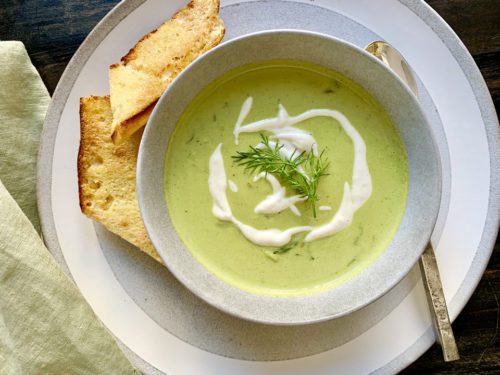 Creamy green soup garnished with herbs, served with toasted bread slices.
