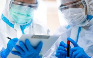 Two healthcare workers in full protective gear reviewing medical data.