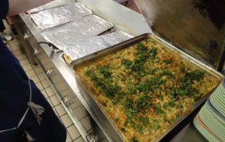 Large tray of baked casserole garnished with chopped herbs in a commercial kitchen.