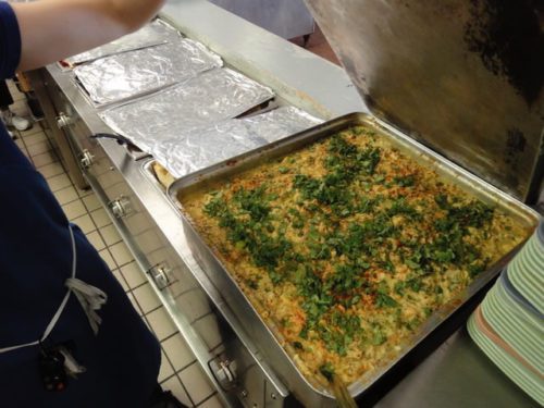 Large tray of baked casserole garnished with chopped herbs in a commercial kitchen.