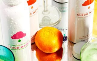 An orange surrounded by bottles of flavored sparkling water on a reflective surface.