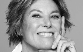 Black and white portrait of a smiling woman with short hair resting her face on her hand.