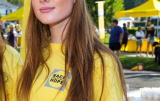Young woman in yellow shirt and cap at an outdoor event.
