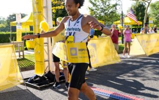 Runner crossing the finish line of a race, smiling with arms outstretched.