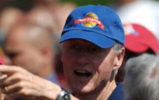 Man wearing a blue baseball cap and speaking outdoors.