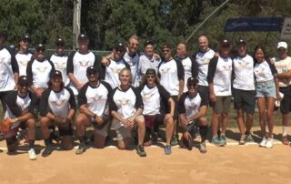 Group photo of a baseball team in matching white and black uniforms outdoors.