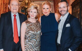 Four well-dressed people posing together at an elegant indoor event.