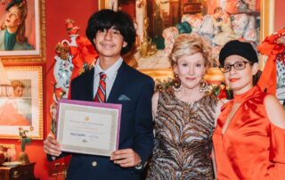 Young man holding certificate with two elegantly dressed women at an event.