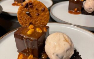 Elegant chocolate dessert with caramel sauce, cookie, and ice cream on a white plate.