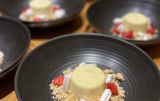 Elegant panna cotta dessert with strawberries and crumbs on black plates.