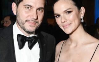 A man in a tuxedo and a woman in an elegant black dress pose together at an event.