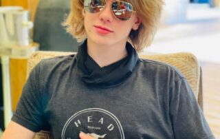 Young person with sunglasses sitting comfortably indoors.