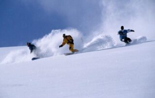 Three snowboarders carving through fresh snow on a sunny slope.
