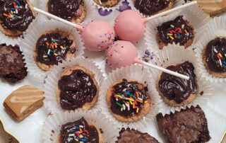 Assorted chocolate treats with sprinkles and pink cake pops on a plate.