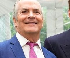 Smiling man in a blue suit and pink tie at an event.