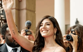 Woman waving at red carpet event.