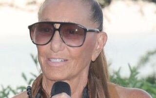 Woman with sunglasses speaking into a microphone outdoors.