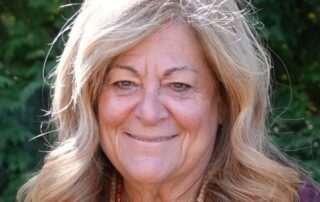 Smiling older woman with long blonde hair outdoors.
