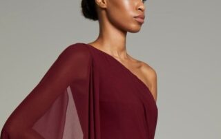 Elegant woman in a one-shoulder burgundy dress with sheer sleeve detail.