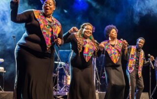 A vibrant choir group performs energetically on stage with colorful scarves.