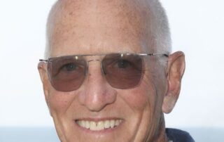 Smiling elderly man wearing sunglasses with a beach background.