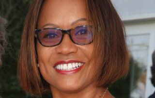 Smiling woman with glasses and short hair outdoors.