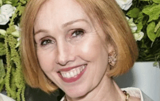 Smiling woman with short blonde hair in front of floral background.