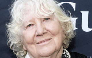 Elderly woman with white curly hair smiling gently.