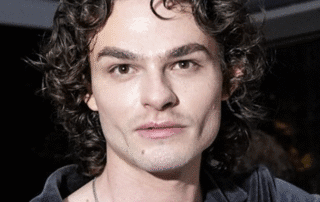 Close-up of a young man with curly hair and defined cheekbones.
