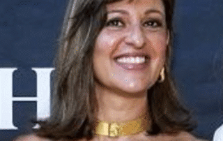 Smiling woman wearing a gold choker and earrings in front of a dark backdrop.