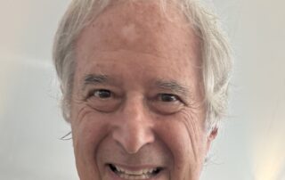 Smiling elderly man with gray hair and a striped shirt.