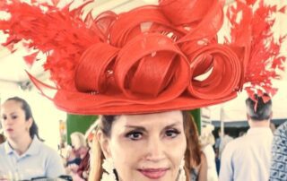 Woman wearing an elaborate red hat and matching dress at an event.