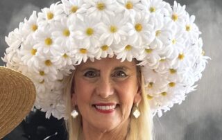 Woman wearing a large hat made of white daisies, smiling.