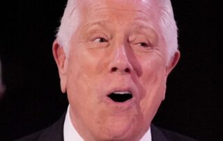 Elderly man in formal wear expressing surprise or excitement.