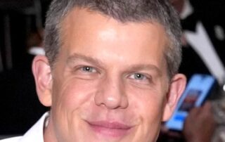 A smiling man with short hair and a white shirt at an event.