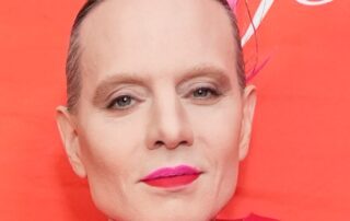 Close-up portrait of a person with slicked-back hair and bold red lipstick.