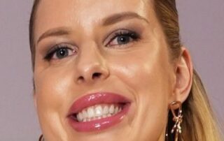 Close-up of a smiling woman with glossy lips and earrings.