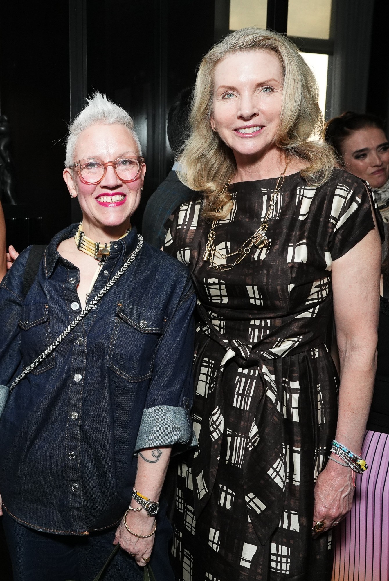 Two women posing at a social event, one in denim and the other in a patterned dress.