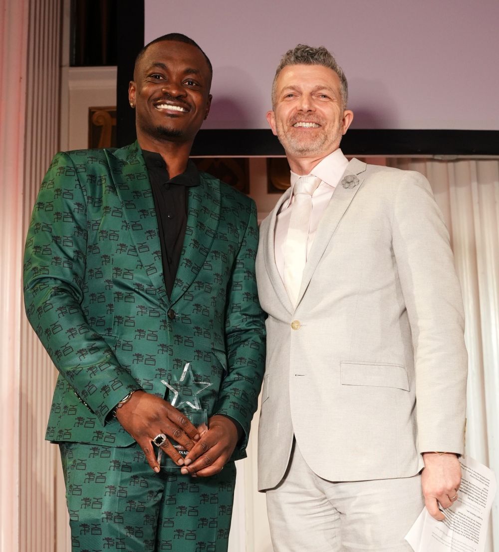 Two men dressed in formal suits smiling at an event.