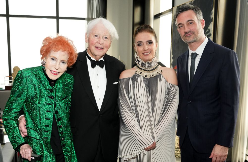 Four elegantly dressed people posing together indoors at a formal event.