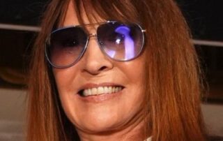 Smiling woman wearing sunglasses with long brown hair.