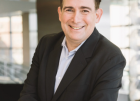 Smiling man in a black suit posing confidently indoors.