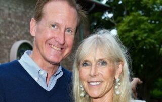 Smiling middle-aged couple posing outdoors near a building and trees.