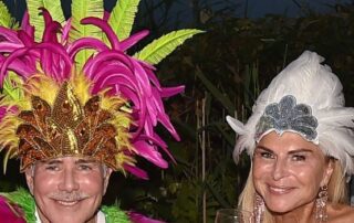 Two people in colorful feathered costumes smiling at an outdoor event.