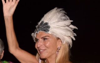 Woman wearing a white feathered headpiece waving at night.
